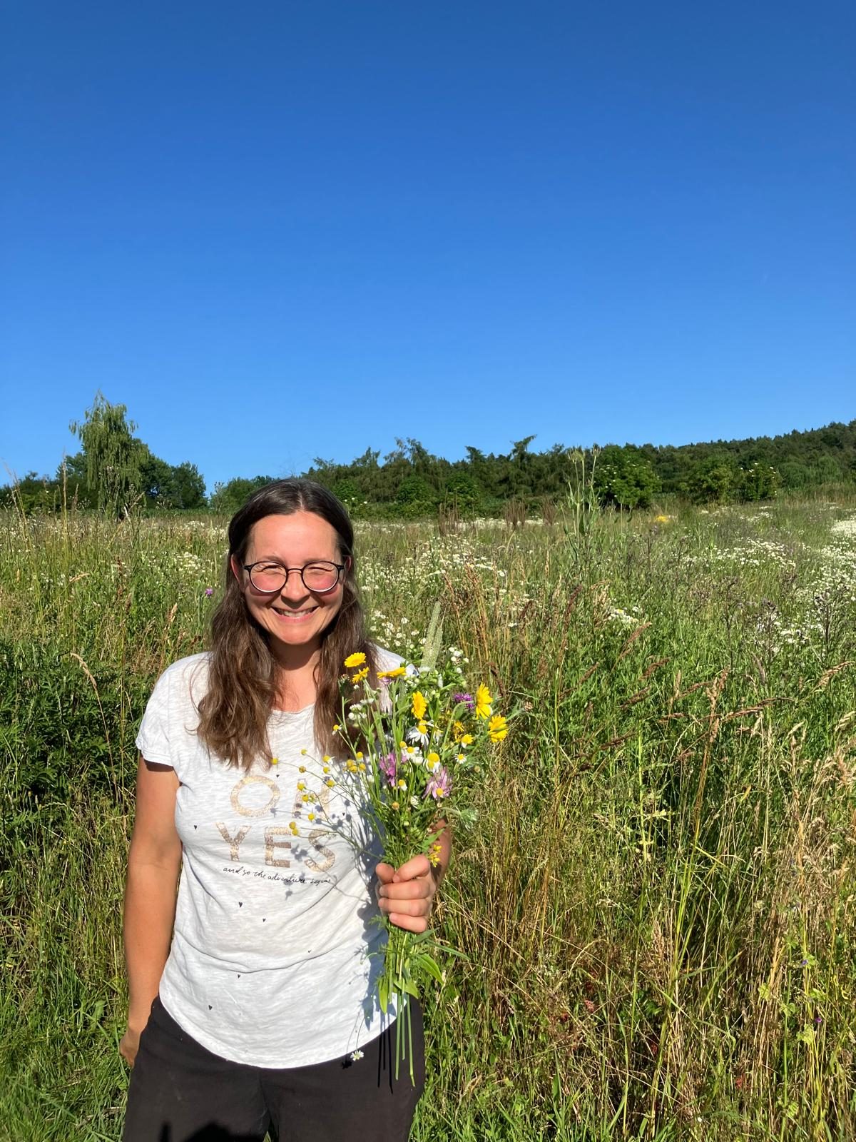 Katja Herzinger auf der Wiese des Bimeshofs mit einem Wildblumenstrauß